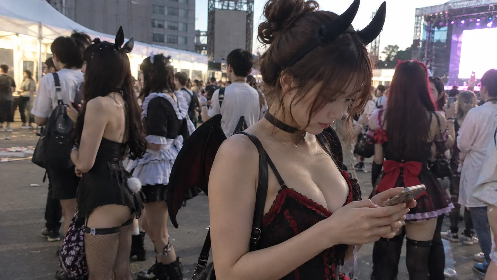 小悪魔コスプレ姿で仮装コスプレ会場におり、スマホを確認している女性